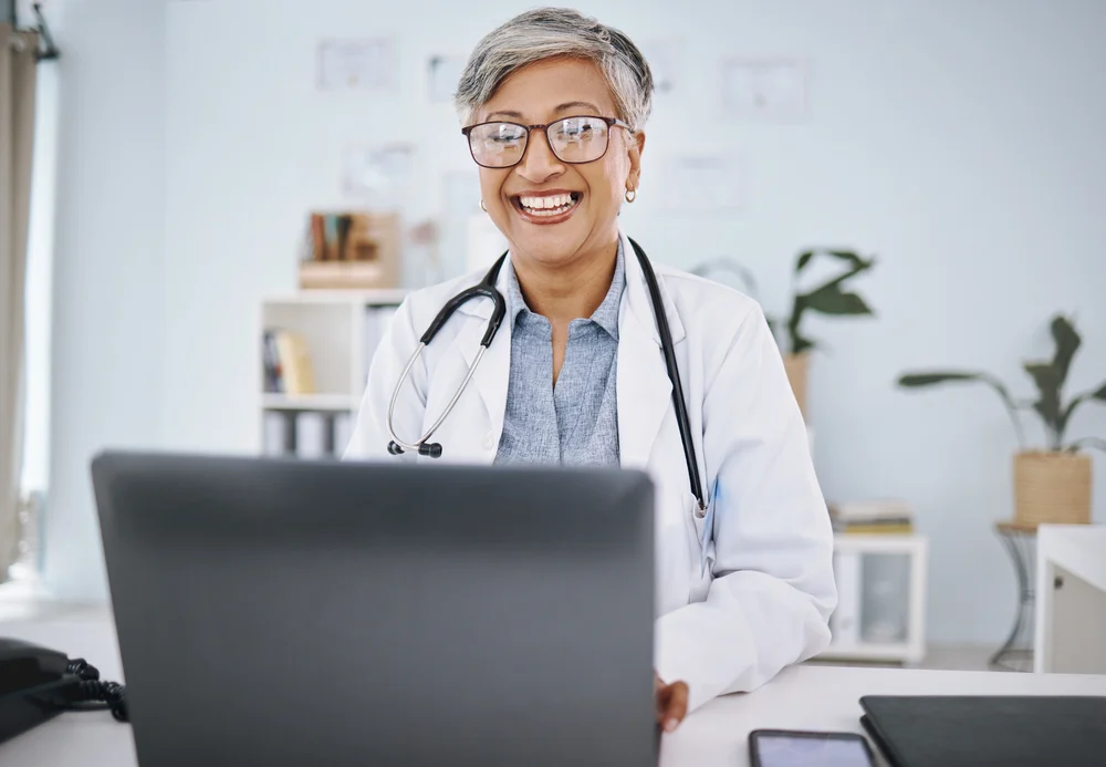 Woman doctor, laptop and happy in hospital office while working online for consultation or research. Medical professional female with internet for advice, healthcare and innovation or management